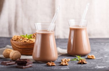 Süt içermeyen organik cevizli çikolatalı süt ve siyah beton arka planda cevizli ahşap tabak. Vejetaryen sağlıklı gıda konsepti, yakın plan, yan görüş.,