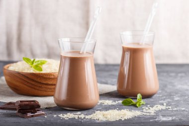 Sütsüz organik pirinç sütlü cam ve siyah beton arka planda pirinç tohumlu ahşap tabakta. Vegan sağlıklı gıda konsepti, yakın çekim, yan görüş, kopyalama alanı.