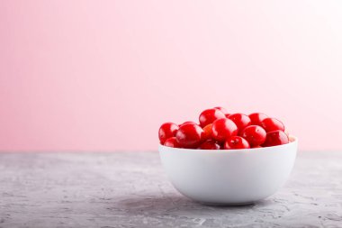 Gri ve pembe arka planda beyaz kasede taze kırmızı kiraz. Yan görünüm, kapat, seçici odak, kopyalama alanı.