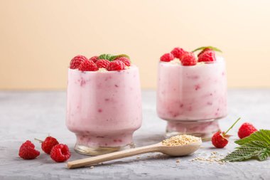 Bardakta ahududu ve susamlı yoğurt ve gri ve turuncu arka planda ahşap kaşık. Yan görünüm, kapat.