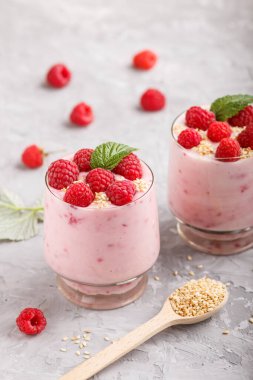 Bardakta ahududu ve susamlı yoğurt ve gri beton arka planda tahta kaşık. Yan görünüm, kapat.