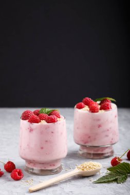 Bardakta ahududu ve susamlı yoğurt ve gri ve siyah arka planda tahta kaşık. Yan görünüm, kapat.