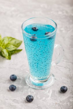 Üzerinde fesleğen tohumu ve gri beton arkaplan olan bir bardak yaban mersini mavisi içecek. Morninig, bahar, sağlıklı içki konsepti. Yan görünüm, kapat.