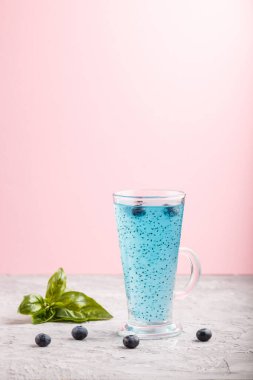 Gri ve pembe arka planda fesleğen tohumlu yaban mersini mavisi bir içecek. Morninig, bahar, sağlıklı içki konsepti. Yan görünüm, boşluk kopyala.