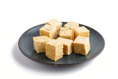 Beyaz arka planda izole edilmiş mavi seramik tabakta geleneksel Hint şekerli soan papdi. Yan görünüm, kapat.