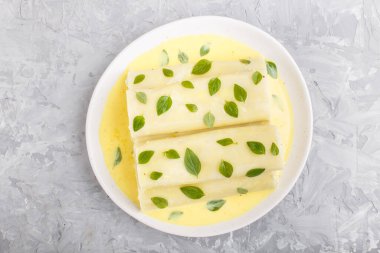 Yumurta soslu Cannelloni makarnası, krem peynir ve gri beton arka planda kekik yaprakları. Üst görünüm, düz görünüm, yakın çekim.