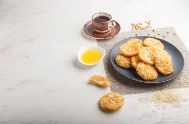 Geleneksel Japon pirinç cipsi kurabiyeleri, ballı ve soya soslu mavi seramik tabak ve beyaz ahşap arka planda bir fincan kahve. Yan görünüm, boşluk kopyala.
