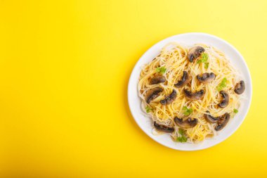 Şampiyon mantarlı pirinç eriştesi, yumurta sosu ve sarı arka planda beyaz seramik tabakta kekik. Üst görünüm, düz görünüm, kopyalama alanı.