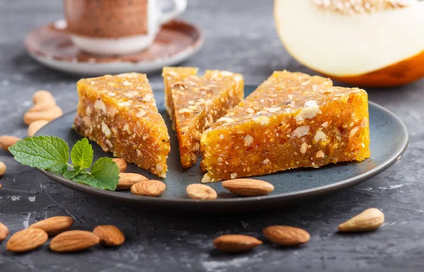 Traditional turkish candy cezerye made from caramelised melon, roasted walnuts, hazelnuts, cashew, pistachios in blue ceramic plate and a cup of coffee on a black concrete background. side view, close up, selective focus.