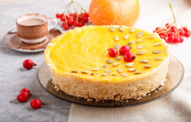 Geleneksel Amerikan balkabağı turtası. Dikenli kırmızı böğürtlen ve balkabağı tohumlarıyla süslenmiş gri beton arka planda bir fincan kahve. Yan görünüm, yakın görünüm, seçici odak.