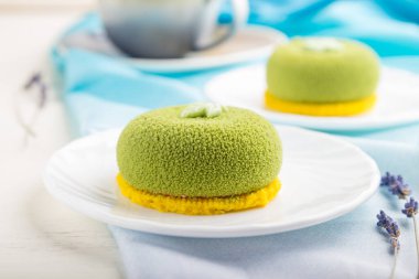 Fıstık kremalı yeşil kremalı kek ve beyaz ahşap arka planda bir fincan kahve ve mavi tekstil. Yan görünüm, yakın görünüm, seçici odak.