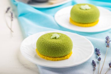 Fıstık kremalı yeşil kremalı kek ve beyaz ahşap arka planda bir fincan kahve ve mavi tekstil. Yan görünüm, yakın görünüm, seçici odak.