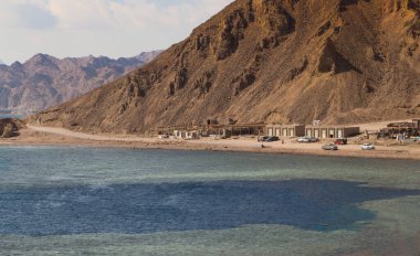 Kızıl Deniz 'in küçük tatil beldeleri ve arka planında dağlar olan kıyı şeridi. Mercan resifi Mavi Delik. Mısır, Sina Yarımadası, Dahab.