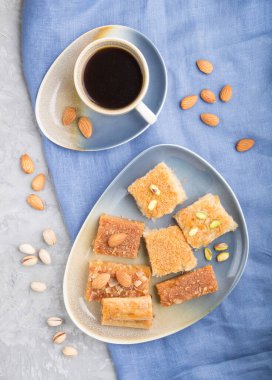 Geleneksel Arap tatlıları (basbus, kunafa, baklava) ve gri beton arka plan ve mavi tekstil üzerinde bir fincan kahve. Üst görünüm, düz görünüm, yakın çekim.