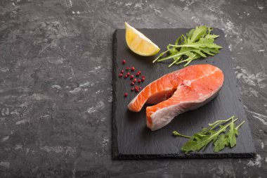 Siyah beton zemin üzerinde roka ve limonlu çiğ somon bifteği. Yan görünüm, kopyala boşluk, kapat.