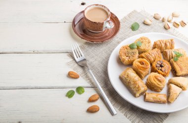 Geleneksel Arap tatlıları (kunafa, baklava) ve beyaz ahşap arka planda bir fincan kahve ve keten tekstil. Yan görünüm, boşluk kopyala.