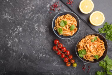 Domates soslu Semolina makarnası, siyah beton arka planda portakal ve otlar. Üst görünüm, düz görünüm, kopyalama alanı.