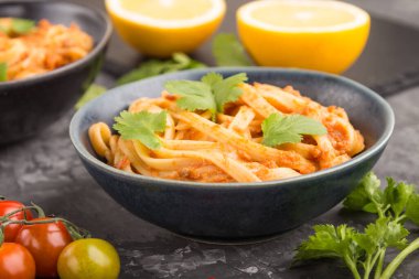 Domates soslu Semolina makarnası, siyah beton arka planda portakal ve otlar. Yan görünüm, yakın görünüm, seçici odak.