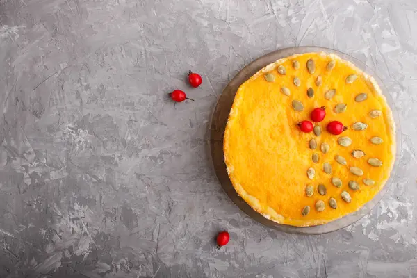 Traditional american sweet pumpkin pie decorated with hawthorn red berries and pumpkin seeds on a gray concrete background. top view, flat lay, copy space.