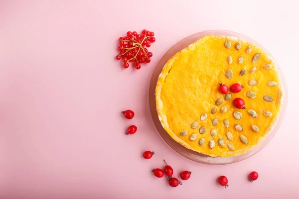 Traditional american sweet pumpkin pie decorated with hawthorn red berries and pumpkin seeds on a pink pastel background. top view, flat lay, copy space.