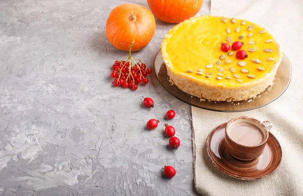 Traditional american sweet pumpkin pie decorated with hawthorn red berries and pumpkin seeds with cup of coffee on a gray concrete background. side view, copy space.