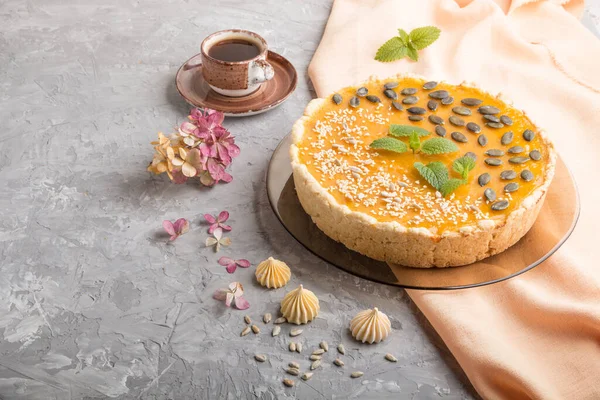 Traditional american sweet pumpkin pie decorated with mint, sesame and pumpkin seeds with cup of coffee on a gray concrete background. side view, copy space.