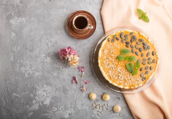 Traditional american sweet pumpkin pie decorated with mint, sesame and pumpkin seeds with cup of coffee on a gray concrete background. top view, flat lay, copy space.