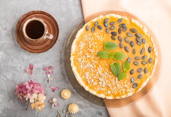 Traditional american sweet pumpkin pie decorated with mint, sesame and pumpkin seeds with cup of coffee on a gray concrete background. top view, flat lay, close up.