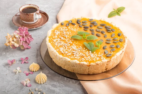 Traditional american sweet pumpkin pie decorated with mint, sesame and pumpkin seeds with cup of coffee on a gray concrete background. side view, close up.