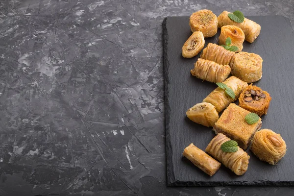 traditional arabic sweets (kunafa, baklava) on a black slate board on a black concrete background. side view, copy space.