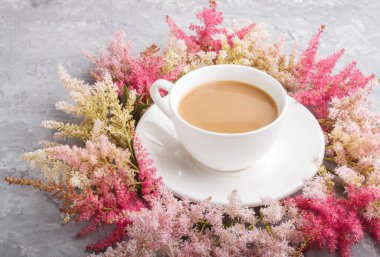 Pembe ve kırmızı astilbe çiçekleri ve gri bir arka planda bir fincan kahve. Morninig, bahar, moda kompozisyonu. Yan görünüm, kapat.