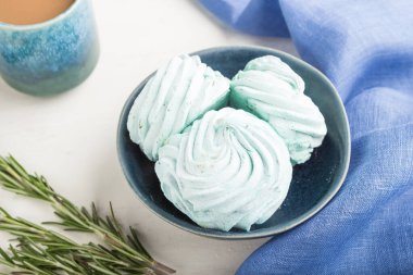 Mavi renkli ev yapımı zephyr ya da mavi tekstil ile beyaz ahşap arka planda bir fincan kahveli marşmelov. Yan görünüm, yakın görünüm, seçici odak.