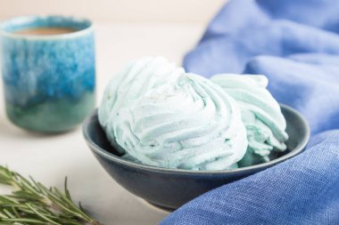 Mavi renkli ev yapımı zephyr ya da mavi tekstil ile beyaz ahşap arka planda bir fincan kahveli marşmelov. Yan görünüm, yakın görünüm, seçici odak.