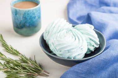 Mavi renkli ev yapımı zephyr ya da mavi tekstil ile beyaz ahşap arka planda bir fincan kahveli marşmelov. Yan görünüm, yakın görünüm, seçici odak.