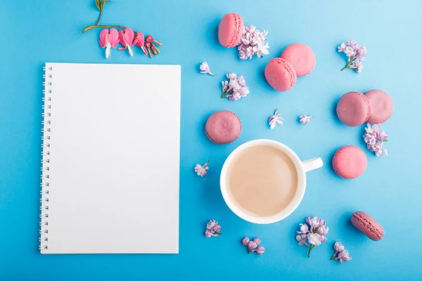 Mor ve pembe badem kurabiyesi ya da defter, kahve, leylak ve pastel mavi arka planda kanayan kalp çiçekleri olan badem kurabiyesi. Morninig, bahar, moda kompozisyonu. Düz yatış, üst görünüm.