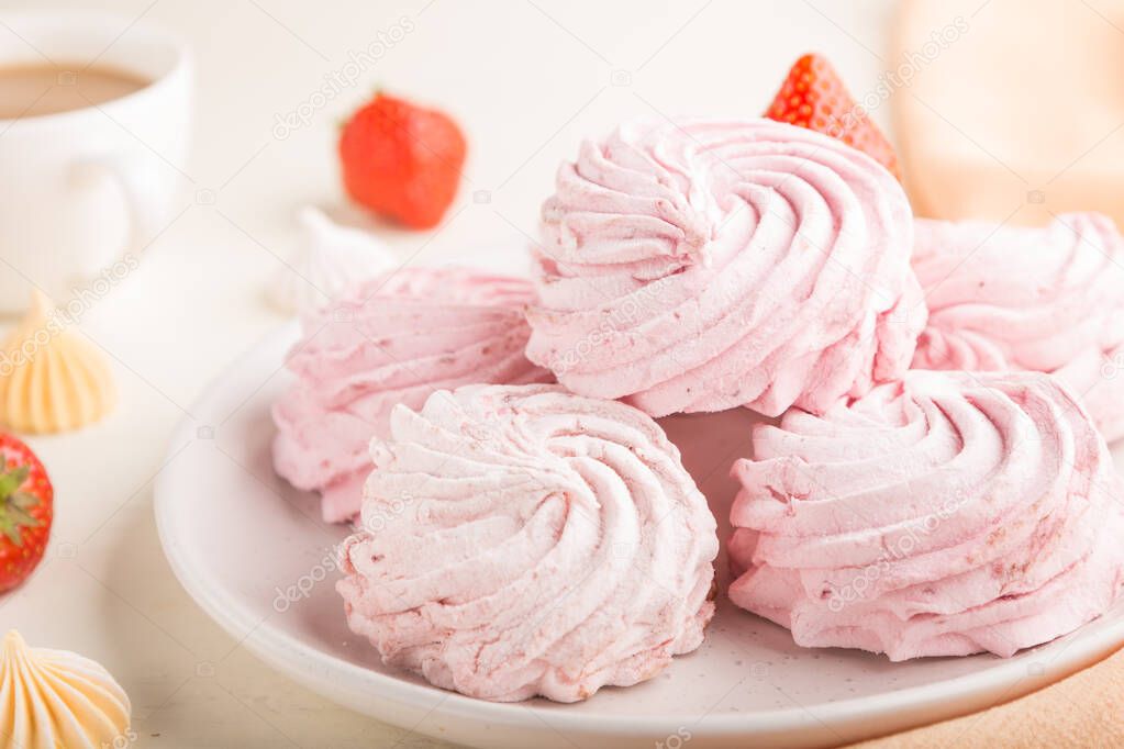 Pink strawberry homemade zephyr or marshmallow with cup of coffee on white wooden background with orange textile. side view, close up, selective focus.