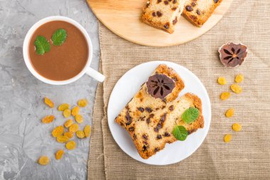 Kuru üzümlü ev yapımı kek, kurutulmuş hurma ve gri beton arka planda bir fincan sıcak çikolata ve keten tekstil. Üst görünüm, düz görünüm, yakın çekim.