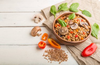 Beyaz ahşap arka plan ve keten tekstil üzerinde ahşap kasede sebze ve mantarlı yulaf lapası. Yan görüş, kopyalama alanı. Rus geleneksel mutfağı.