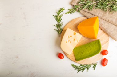 Yeşil fesleğen peyniri ve beyaz ahşap arka planda biberiye ve domatesli çeşitli peynir çeşitleri. Üst görünüm, kopyalama alanı, seçici odak.