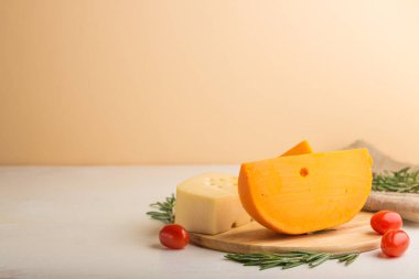 Beyaz ve turuncu arka plan ve keten tekstil üzerine ahşap tahtada biberiyeli ve domatesli çeşitli peynir çeşitleri. Yan görünüm, kapat, boşluğu kopyala, seçici odak.