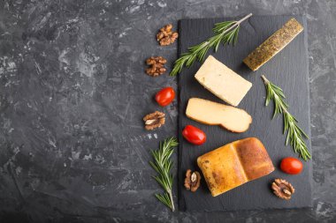 Tütsülenmiş peynir ve siyah beton arka planda siyah tahtada biberiyeli ve domatesli çeşitli peynirler. Üst görünüm, kopyalama alanı, düz uzanma.