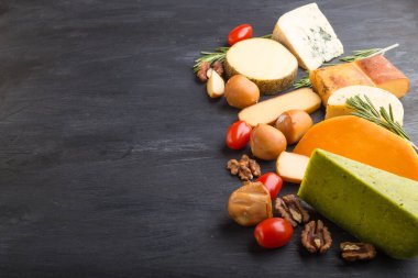 Siyah ahşap arka planda biberiyeli ve domatesli farklı peynir çeşitleri. Yan görünüm, kapat, boşluğu kopyala.