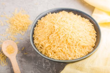 Çiğ altın pirinçli mavi seramik kâse ve gri beton arka planda ahşap kaşık ve sarı tekstil. Yan görünüm, yakın görünüm, seçici odak.