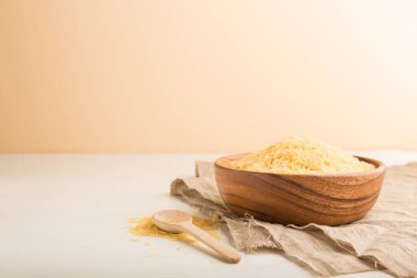 Tahta kase, çiğ altın pirinç, beyaz ve turuncu arka planda ahşap kaşık ve keten tekstil. Yan görünüm, kopyalama alanı, seçici odak.