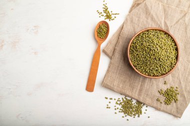 Tahta kase, çiğ yeşil fasulye çekirdeği ve beyaz arka planda ahşap kaşık ve keten tekstil. Üst görünüm, düz görünüm, kopyalama alanı.