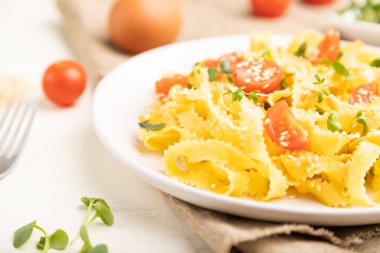 Beyaz ahşap arka planda domates, yumurta, susam ve mikroyeşil lahanalı Reginelle irmik makarna ve keten tekstil. Yan görünüm, yakın görünüm, seçici odak.