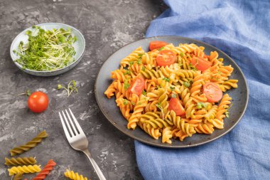 Siyah beton arka plan ve mavi tekstil üzerinde domates ve mikroyeşil lahanalı Tortiglioni irmik makarna. Yan görünüm, kapat, boşluğu kopyala.
