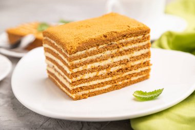 Kremalı ev yapımı ballı kek ve gri beton arka planda bir fincan kahve ve yeşil tekstil. Yan görünüm, yakın görünüm, seçici odak.