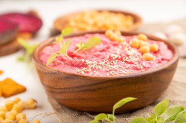 Beyaz ahşap bir arka plan ve keten tekstil üzerinde pancar ve mikroyeşil fesleğenli humus. Yan görünüm, yakın görünüm, seçici odak.