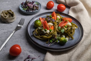 Tagliatelle yeşil ıspanaklı domates, bezelye ve mikroyeşil lahanalı gri beton arka plan ve keten tekstil. Yan görünüş, yaklaş, sert ışık.